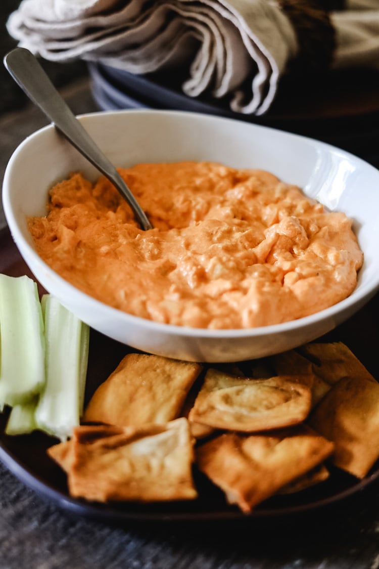 buffalo chicken dip in a bowl with pita chips and celery sticks