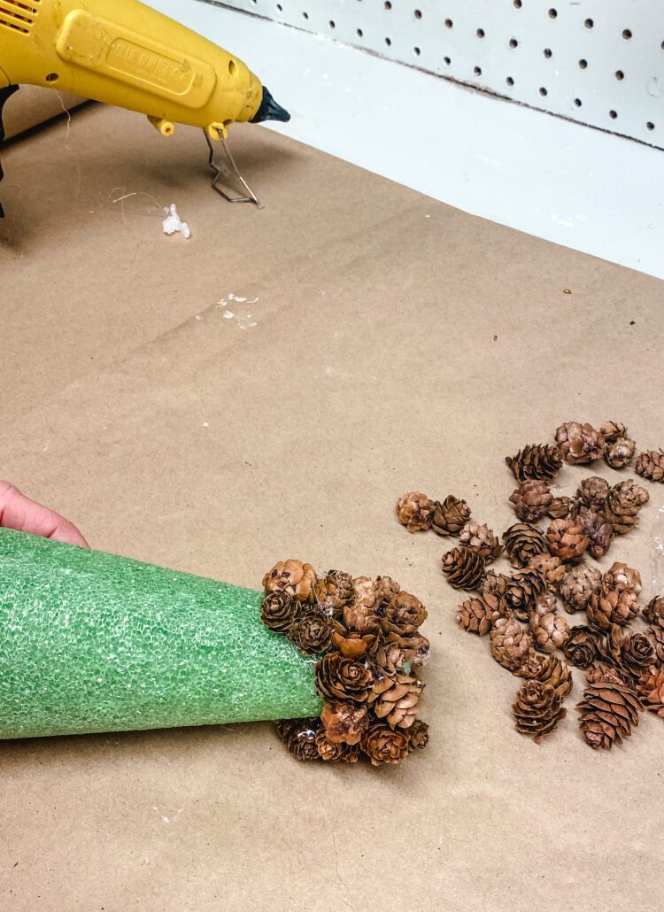hot gluing pine cones onto a foam cone