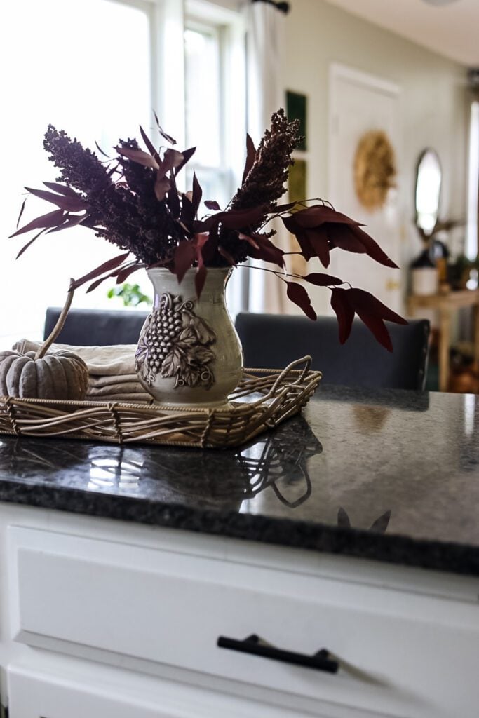 a kitchen counter with a tray that is holding a pumpkin and a vase filled with red branches