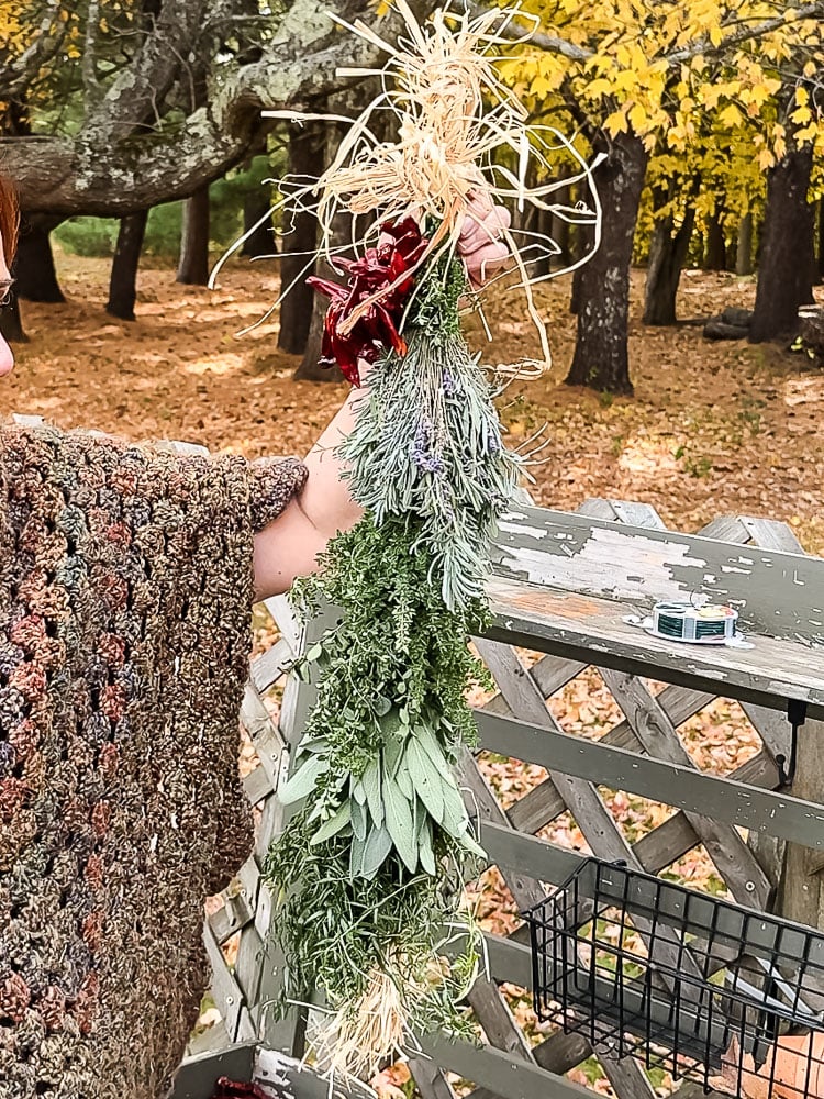 woman holding up a fresh herb swag outside with fall foliage behind her