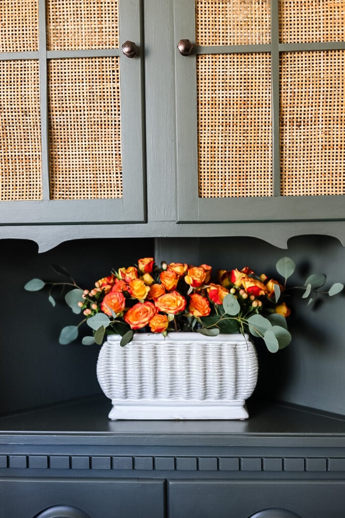 orange roses in white container on green hutch