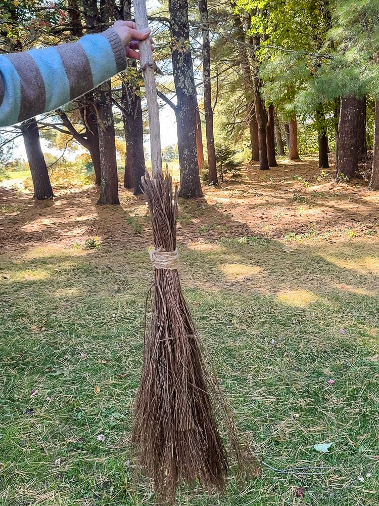 woman holding a witch broom outside with woods in the background