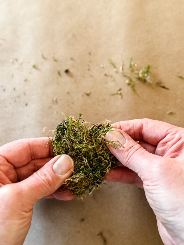 hands securing moss to a grapevine heart
