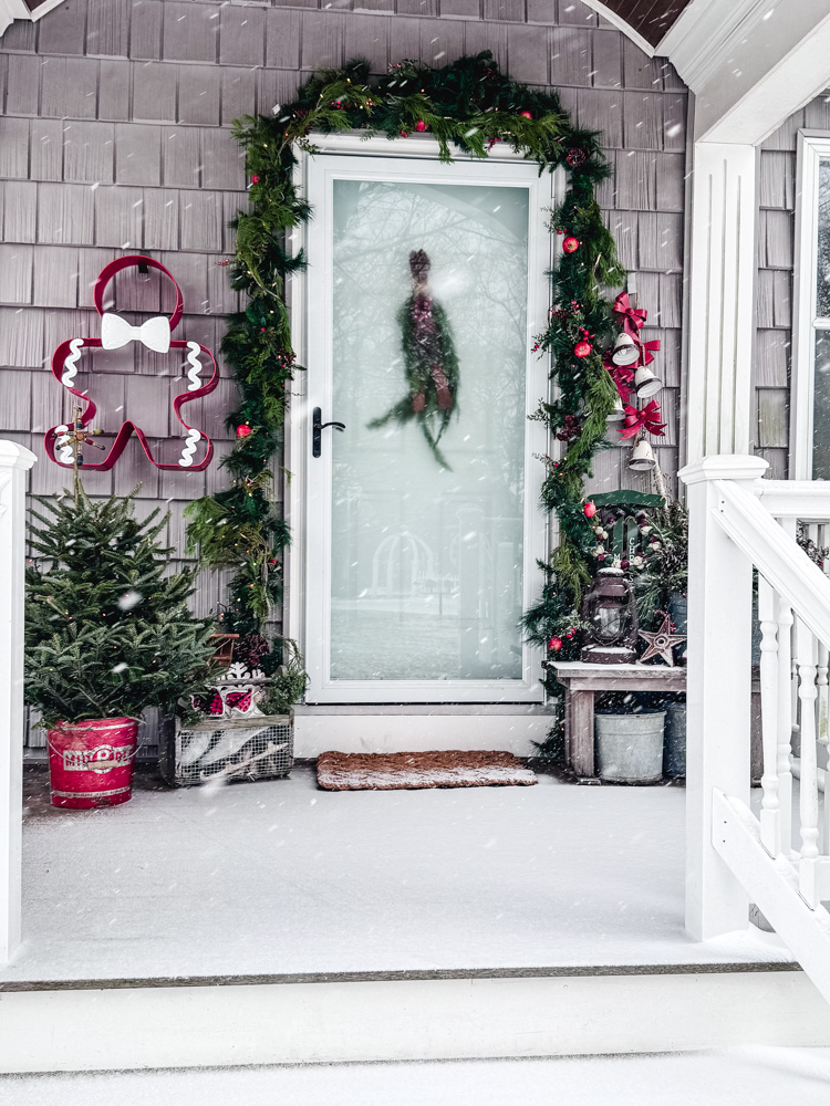 front porch decorated for christmas with garland, tree, and gingerbread wall hanging