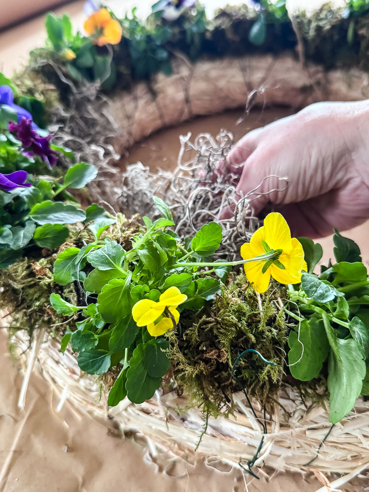 a woman's hand adding moss to a wreath