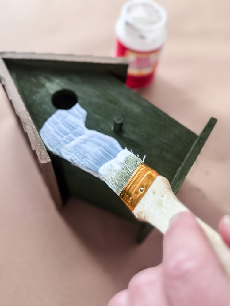 applying mod podge to a wooden birdhouse