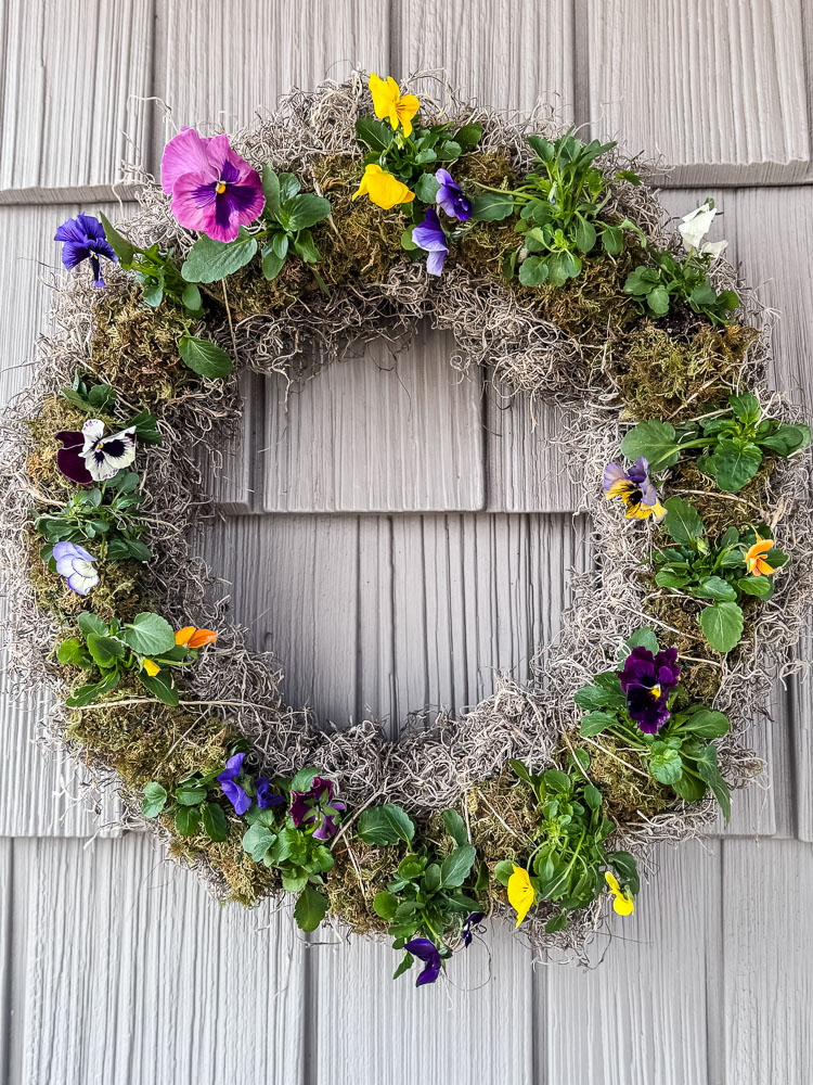 live pansy wreath hanging on a house with gray siding