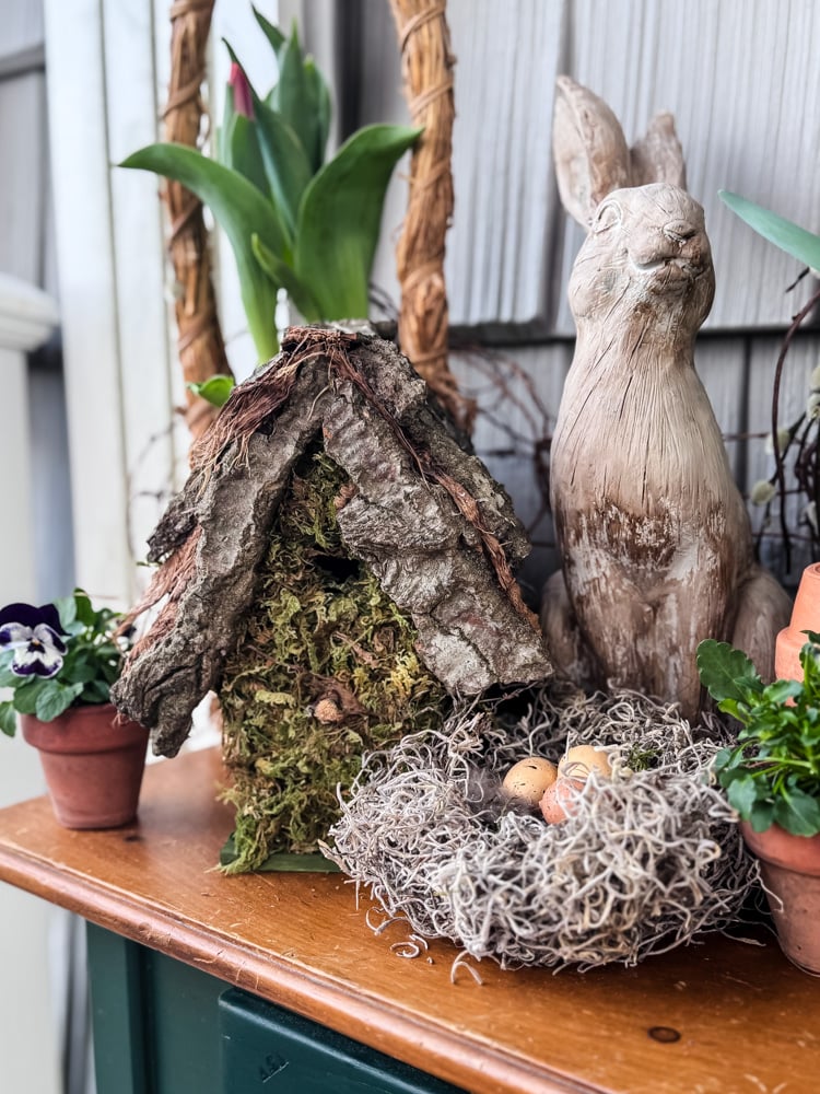 a table with spring natural looking spring decorations like a bird nest and birdhouse, with pot of tulips and a bunny statue