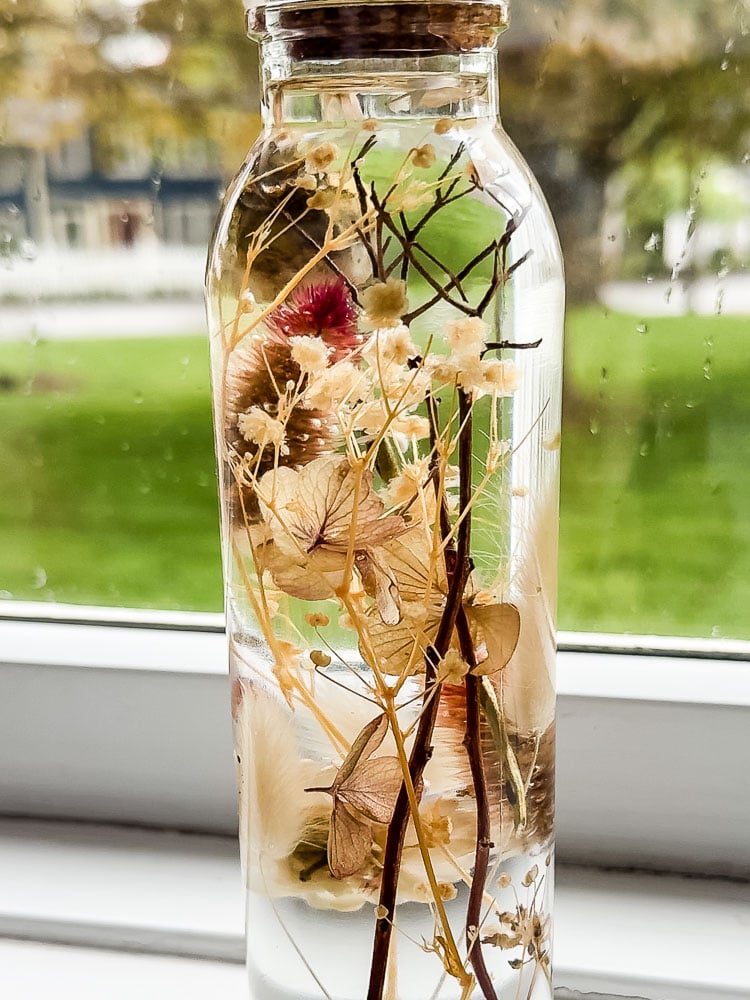 a herbarium bottle in a white windowsill with green grass outside of it.