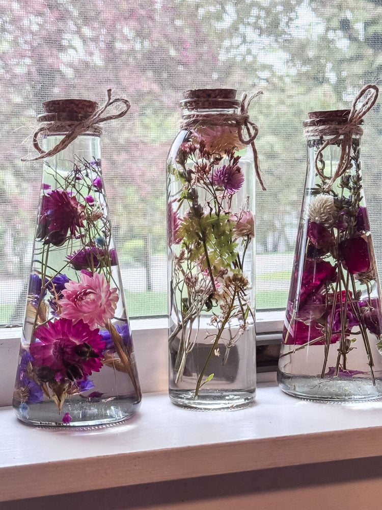 glass bottles with flowers suspended in oil in window