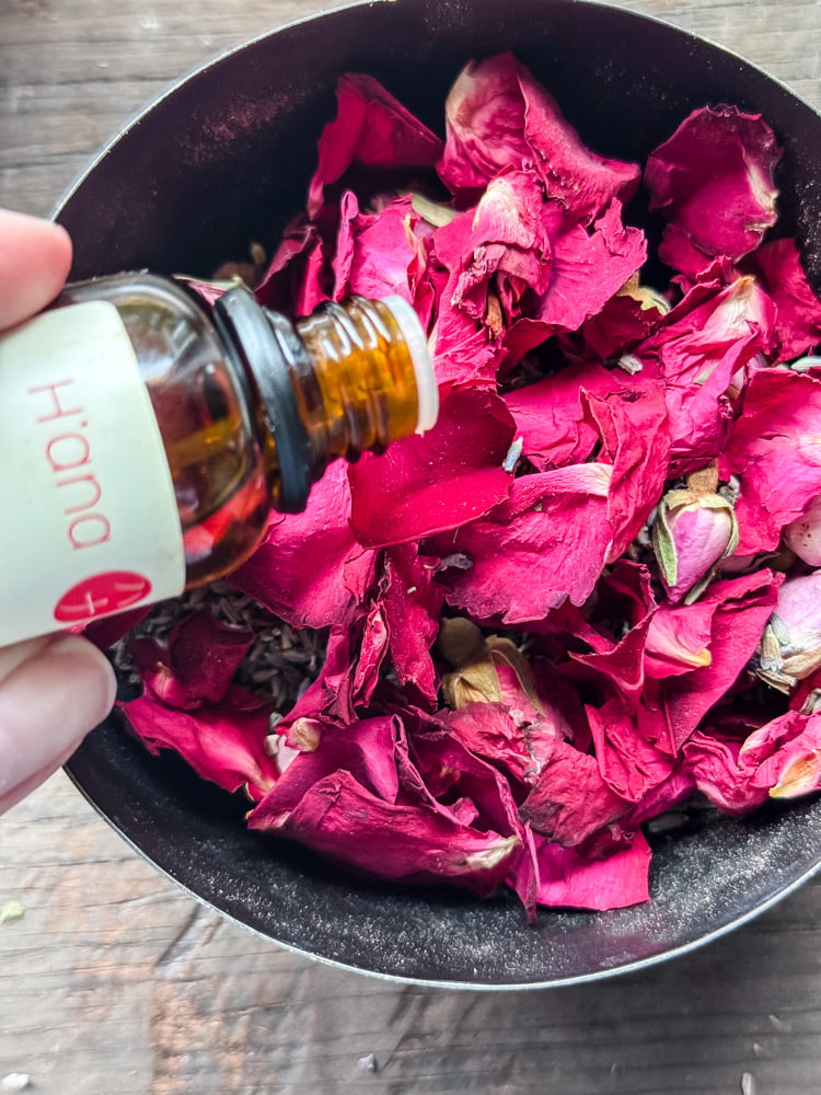 adding rose oil to a bowl of rose petals