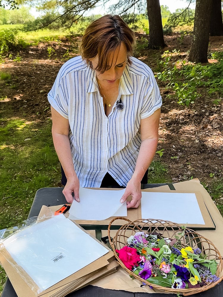 woman using a flower press outside with trees behind her and a field