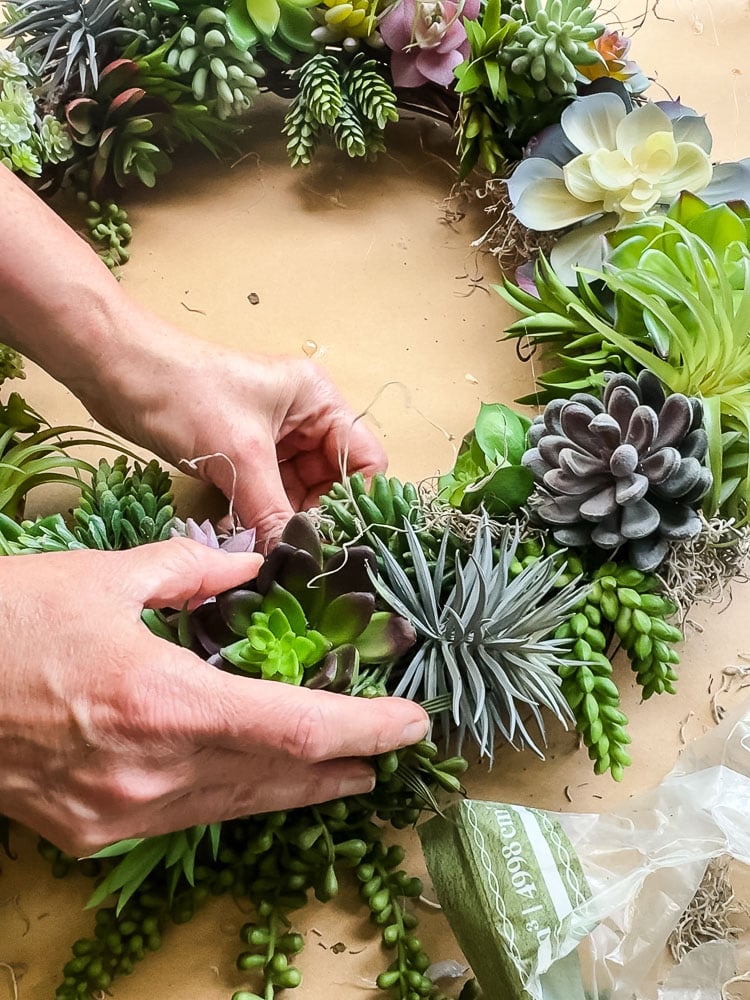 woman's hands adding spanish moss to a diy succulent wreath project