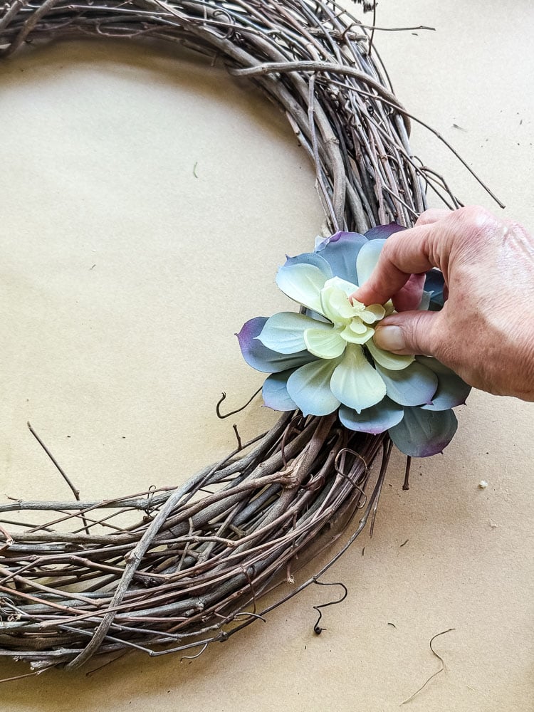 a hand gluing a faux succulent to a wreath