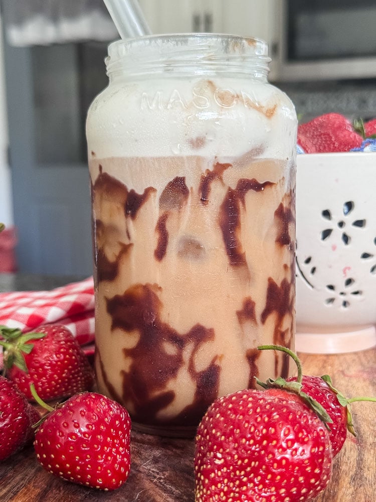 a decadent iced coffee in a mason jar with strawberry cold foam