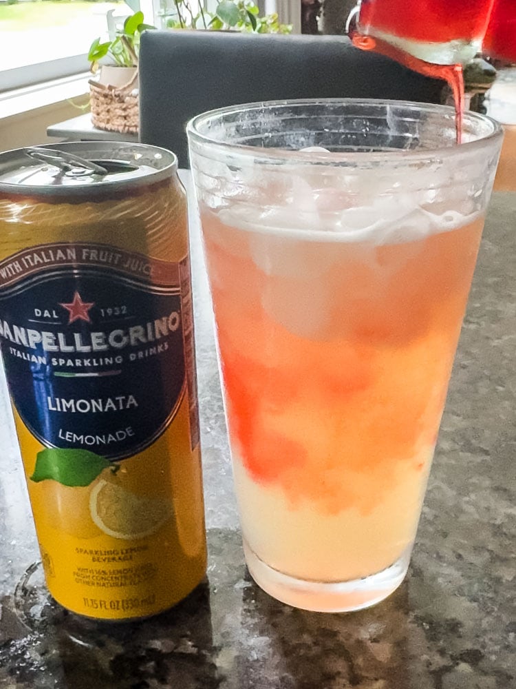 san pellagrino lemonade can and glass of lemonade with strawberry syrup being poured over