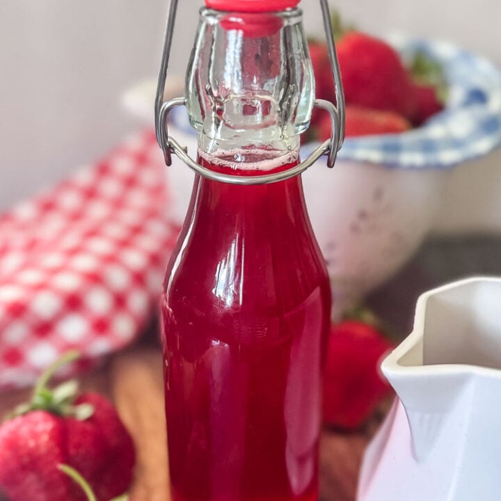 a bottle of red strawberry syryp styled with berries and red napkin and bowl of strawberries
