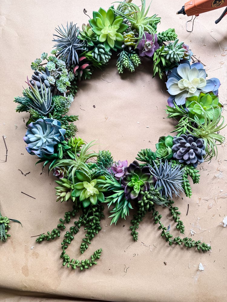 artificial succulent wreath on brown kraft paper with a glue gun in view