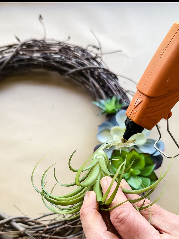 hot glue gun gluing a fake succulent to a wreath