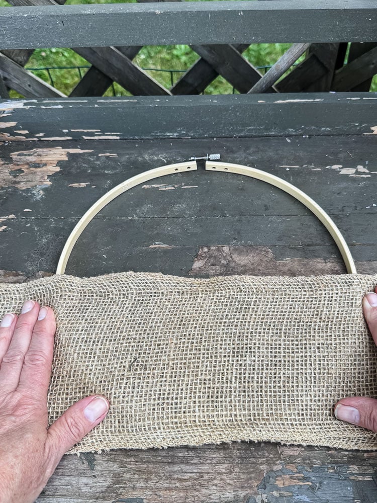 an embroidery hoop and a hand holding wide burlap ribbon on top