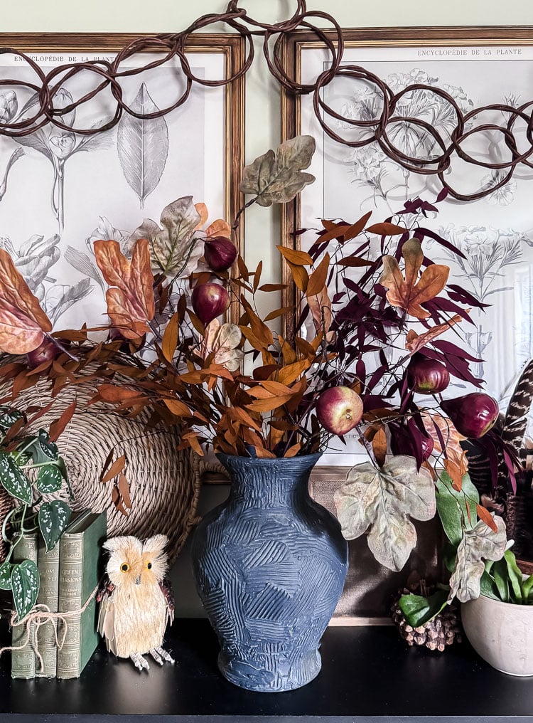 a mantel styled for autumn with a large navy vessel filled with fall branches and leaves